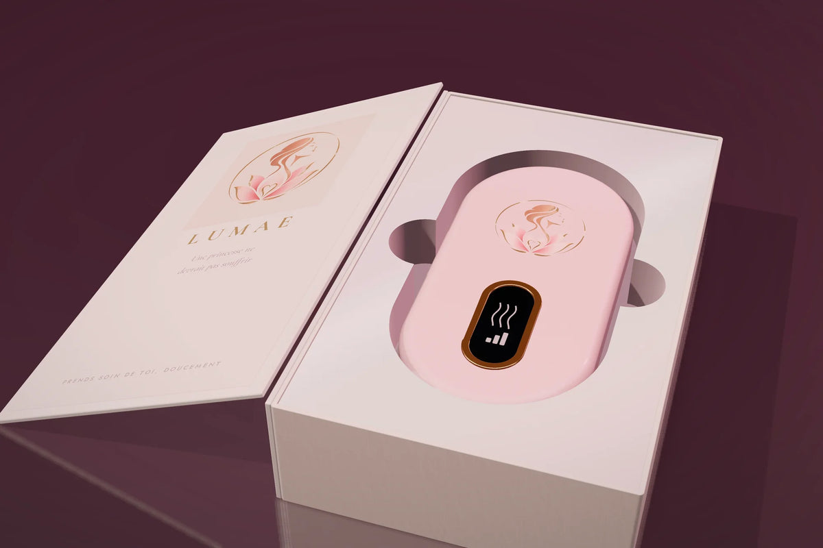 Le coffret Lumae ouvert comme un livre, la ceinture chauffante rose poudré dans son écrin nacré.